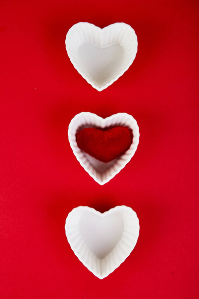 Corazones de cerámica blanca con corazones de felpa roja sobre fondo rojo. Composición plana. Romántico, San Valentín concepto del día. Amor. Copiar espacio. - Foto, Imagen