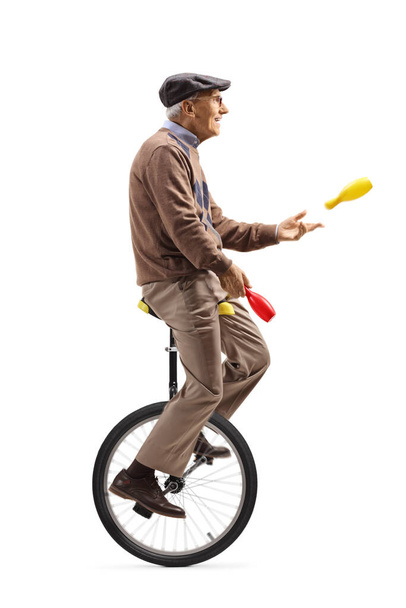 Elderly man a riding a unicycle and juggling isolated on white background - Foto, immagini