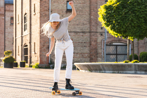 Stylish  girl trying to ride a longboard on a city street - Valokuva, kuva