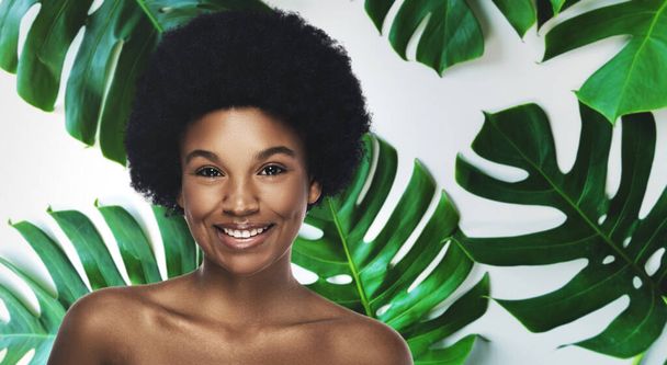 Young and beautiful African woman with perfect smooth skin in tropical leaves. Concept of natural cosmetics and skincare. - Φωτογραφία, εικόνα