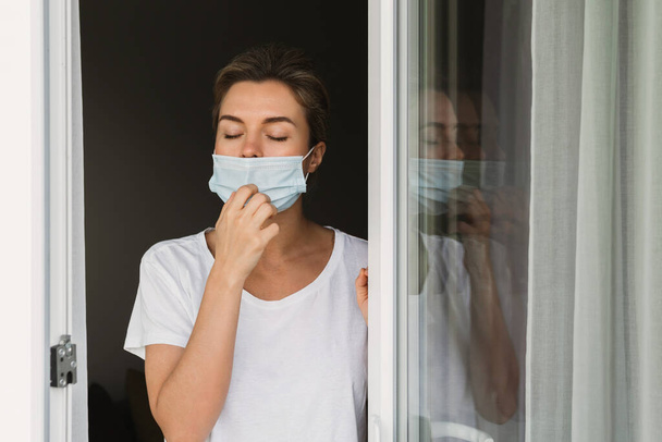 Young woman is going on a balcony to take a deep breath because was using prevention mask for all day long - Foto, immagini
