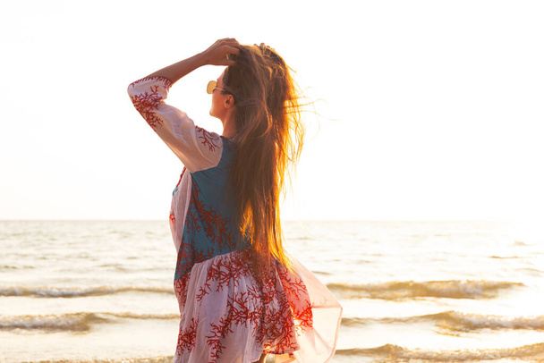 Young lovely woman wearing beautiful dress  is walking by the sea shore during sunset - Foto, afbeelding