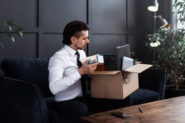 Young man getting fired from his job. Businessman and cardboard box with his personal belongings from a workplace. - Foto, Bild