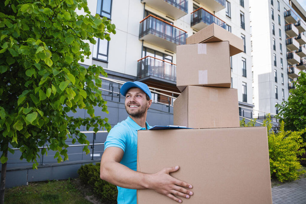Strong delivery man holding a stack of a cardboard boxes on a city street - Photo, Image