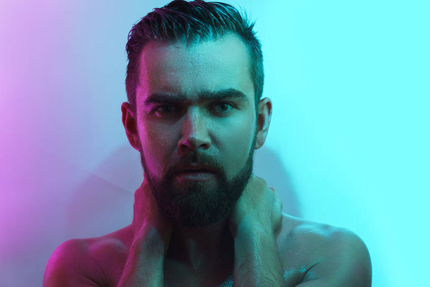Portrait of handsome young man with wet skin in neon light - Фото, изображение
