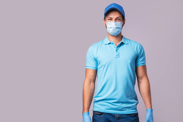 Jovem vestindo uniforme azul com máscara de prevenção e luvas isoladas em fundo cinza - Foto, Imagem