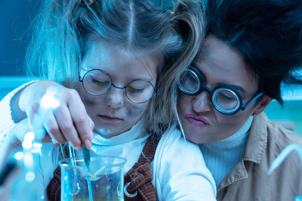 Funny teacher and little girl during chemistry lesson mixing chemicals in a laboratory - Foto, Imagem
