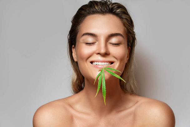 CBD cosmetics concept. Beautiful woman with a cannabis leaf on gray background - Foto, immagini