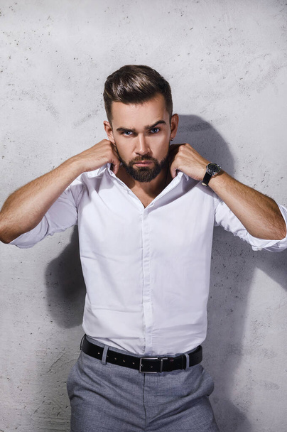Portrait of handsome  bearded man wearing white shirt is posing against concrete wall - Photo, Image