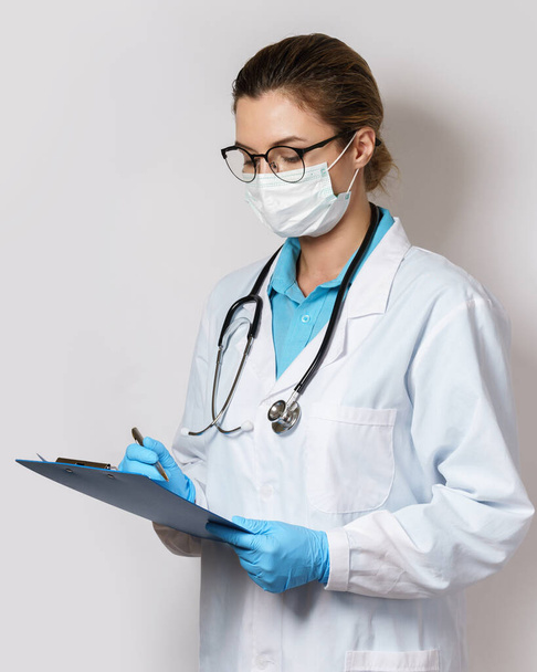 Young female doctor filling a report on gray background - Foto, Imagen