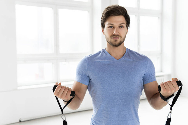 Young handsome man during workout with a resistance rubber bands in the gym. Biceps curls exercise. - Fotoğraf, Görsel