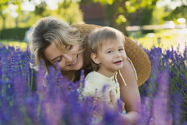 Beautiful and young woman with her cute little son in a lavender field - Фото, изображение