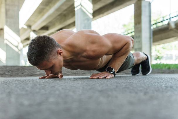 Young and muscular man is doing push-ups during calisthenic workout on a street - Φωτογραφία, εικόνα