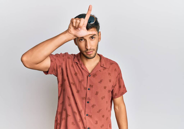 Jonge knappe man draagt casual zomer kleren maken van mensen met vingers op het voorhoofd doen verliezer gebaar bespotten en beledigend.  - Foto, afbeelding
