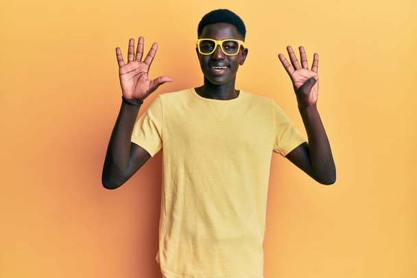 Genç Afro-Amerikan adam günlük kıyafetler ve gözlük takıyor ve dokuz numaralı parmaklarıyla işaret ediyor ve gülümsüyor kendinden emin ve mutlu..  - Fotoğraf, Görsel