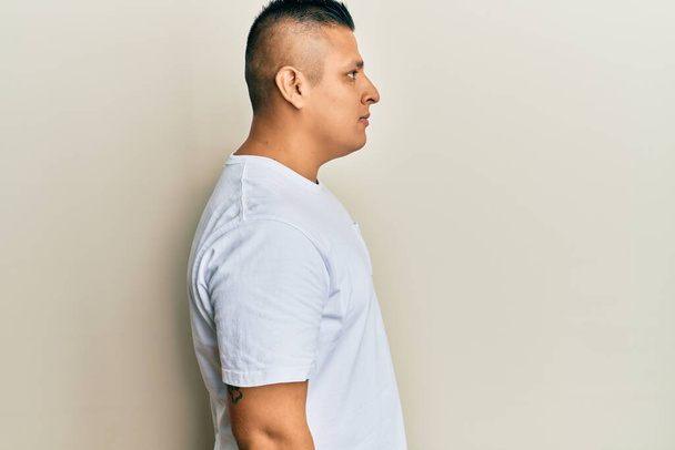 Fiatal latin férfi visel alkalmi fehér póló látszó oldalra, relax profil pózol természetes arc magabiztos mosollyal.  - Fotó, kép