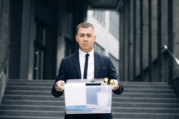 Portrait sad male office worker in depression with box of personal stuff. Businessman lost job. Fired man outdoors. Depressed jobless person. Unemployment concept. Left without money - Foto, Bild