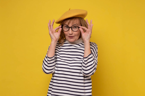 Mujer de mediana edad con sombrero amarillo y gafas sonrientes mirando a la cámara. - Foto, imagen