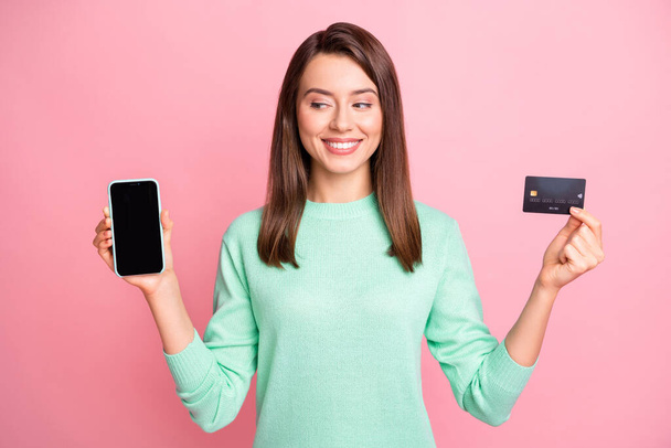 Photo of lady hold telephone look screen empty space credit card toothy smile wear turquoise sweater isolated pink color background - Fotó, kép