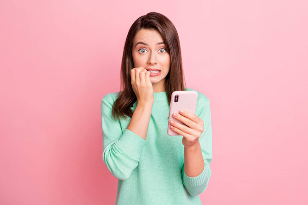 Photo of worried girl hold telephone gnaw bite fingernails look camera wear turquoise sweater isolated pink color background - Foto, Imagen