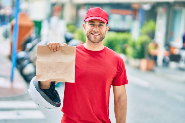 Fiatal fehér futár mosolyog boldog gazdaság szállítási papírzacskó a városban. - Fotó, kép
