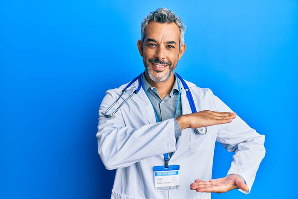 Middle age grey-haired man wearing doctor uniform and stethoscope gesturing with hands showing big and large size sign, measure symbol. smiling looking at the camera. measuring concept.  - Foto, Imagem