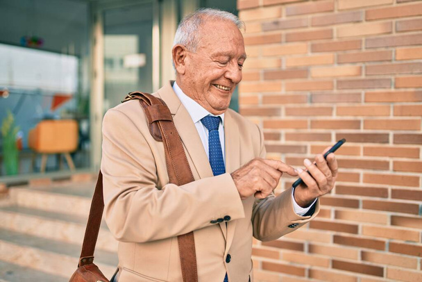 Senior grey-haired businessman smiling happy using smartphone at the city. - 写真・画像