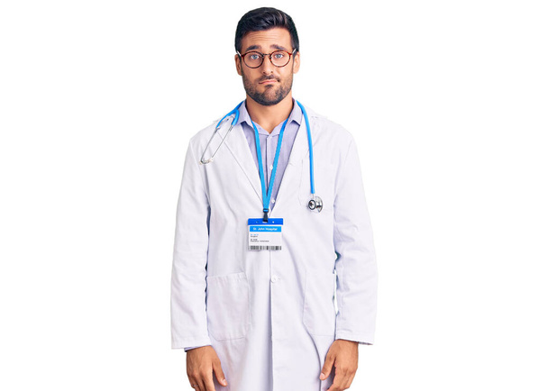 Young hispanic man wearing doctor uniform and stethoscope looking sleepy and tired, exhausted for fatigue and hangover, lazy eyes in the morning.  - Foto, imagen