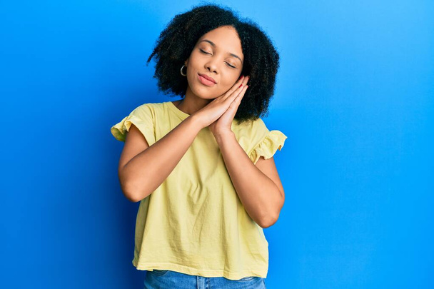Junge afrikanisch-amerikanische Mädchen in lässiger Kleidung schlafen müde träumen und posieren mit den Händen zusammen, während sie mit geschlossenen Augen lächeln.  - Foto, Bild