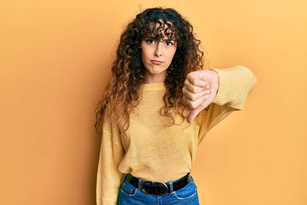 Young hispanic girl wearing casual clothes looking unhappy and angry showing rejection and negative with thumbs down gesture. bad expression.  - Фото, изображение