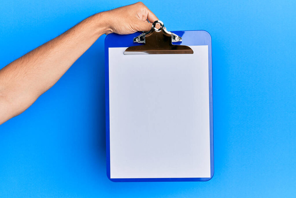 Young hispanic hand holding clipboard over isolated blue background. - Φωτογραφία, εικόνα