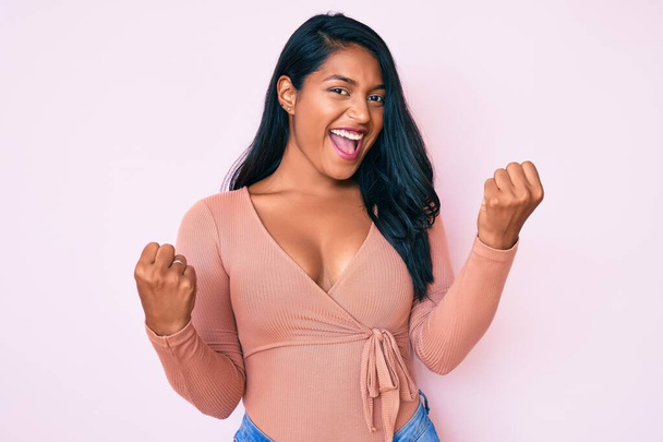 Beautiful latin young woman with long hair wearing casual clothes screaming proud, celebrating victory and success very excited with raised arms  - Photo, Image