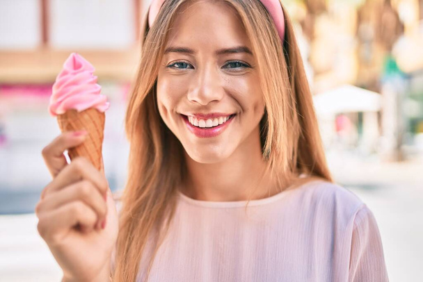 Νεαρή λευκή κοπέλα χαμογελά χαρούμενη τρώγοντας παγωτό στην πόλη. - Φωτογραφία, εικόνα