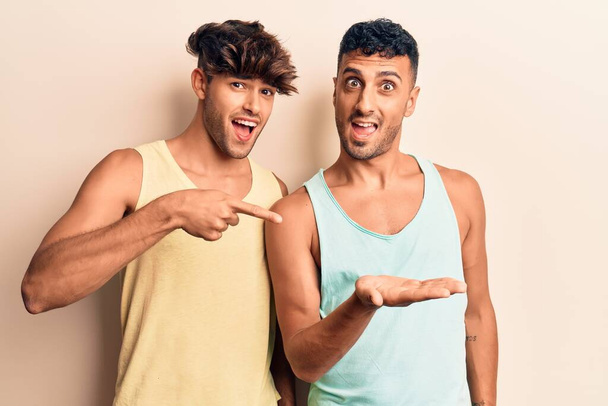 Mladý gayové pár nosí ležérní oblečení ohromen a usmívá se do kamery, zatímco prezentuje s rukou a ukazuje prstem.  - Fotografie, Obrázek