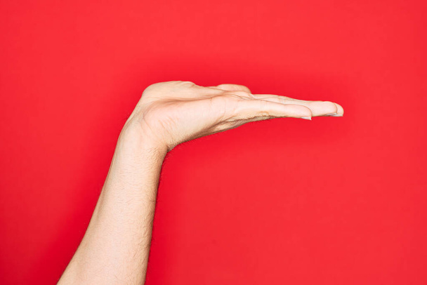 Hand of caucasian young man showing fingers over isolated red background with flat palm presenting product, offer and giving gesture, blank copy space - Foto, Imagem