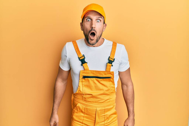 jovem bonito homem vestindo handyman uniforme sobre amarelo fundo medo e chocado com surpresa e espantado expressão, medo e animado rosto.  - Foto, Imagem