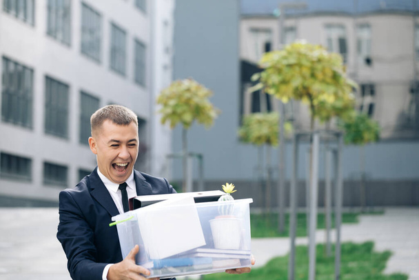 Happy businessman walking the street with box of stuff as leaving business center and dancing. Male office worker leaving job and celebrating. Fired cheerful man. Great day, good mood - Photo, Image