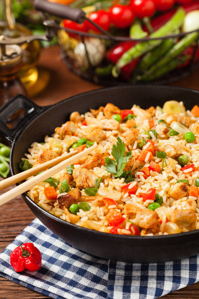 Fried rice with chicken. Prepared and served in a wok. Natural wood in the background. Front view. - Foto, Imagen