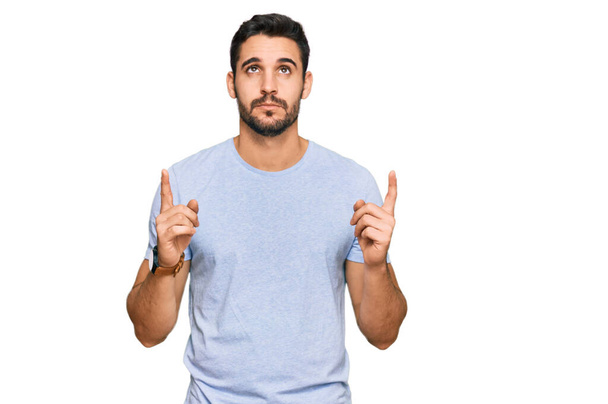 Young hispanic man wearing casual clothes pointing up looking sad and upset, indicating direction with fingers, unhappy and depressed.  - Photo, image