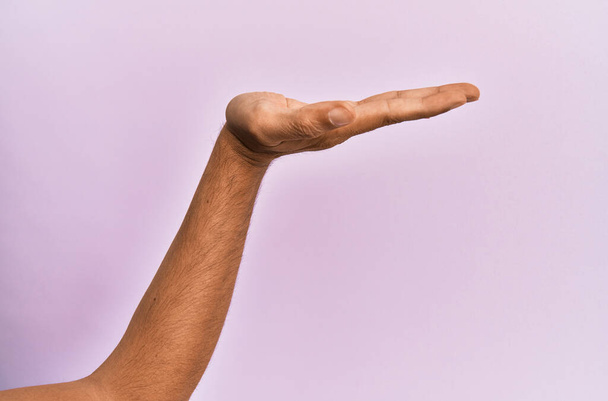 Bras et main de jeune homme caucasien sur fond rose isolé avec paume plate présentant produit, offre et geste, espace de copie vierge  - Photo, image