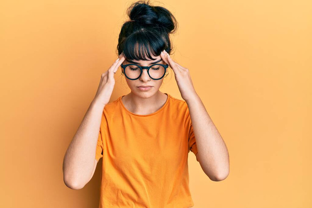 Junge hispanische Mädchen in lässiger Kleidung und Brille leiden unter Kopfschmerzen verzweifelt und gestresst, weil Schmerzen und Migräne. Hände auf den Kopf.  - Foto, Bild