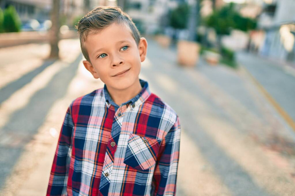 Αξιολάτρευτο καυκάσιο αγόρι χαμογελά χαρούμενος στέκεται στην πόλη. - Φωτογραφία, εικόνα