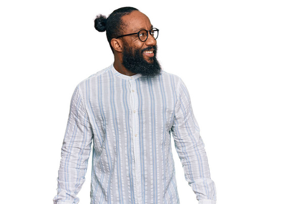 Fiatal afro-amerikai férfi, aki üzleti inget és szemüveget visel, és mosollyal az arcán néz félre, természetes kifejezéssel. nevetés magabiztos.  - Fotó, kép