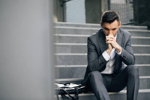 Upset young businessman in frustration outside office department. Fired unhappy caucasian bearded man losing job crying and sitting on stairs. Unemployment. Crisis - Φωτογραφία, εικόνα