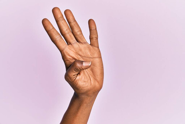 Arm und Hand einer schwarzen Frau mittleren Alters über rosa isoliertem Hintergrund, Zählzahl 4, die vier Finger zeigt  - Foto, Bild