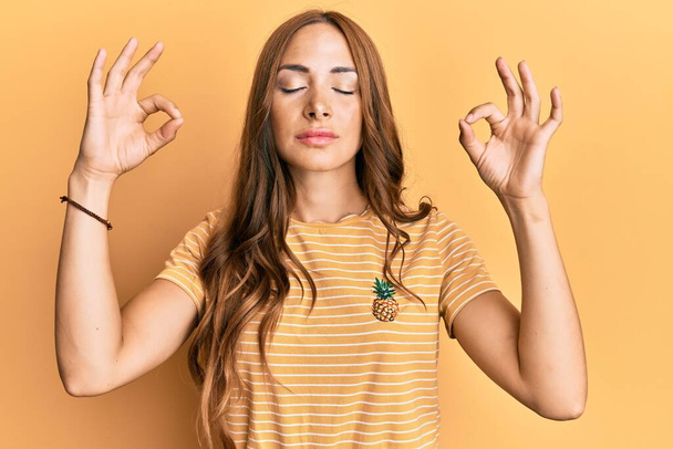 Jeune femme brune portant des vêtements décontractés se détendre et sourire les yeux fermés en faisant un geste de méditation avec les doigts. concept de yoga.  - Photo, image