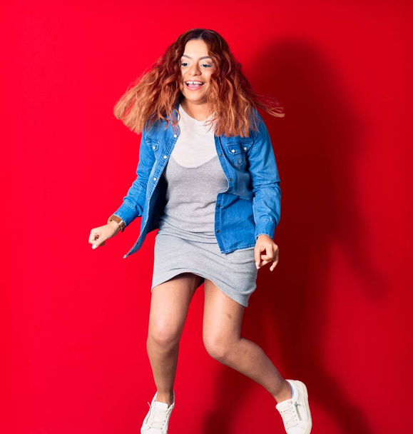 Young beautiful latin woman wearing casual clothes smiling happy. Jumping with smile on face over isolated red background - Foto, afbeelding