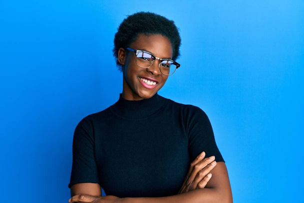 Chica afroamericana joven con ropa casual y gafas cara feliz sonriendo con los brazos cruzados mirando a la cámara. persona positiva.  - Foto, Imagen