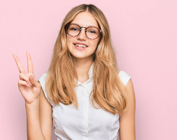 Красивая юная кавказская девушка в повседневной одежде и очках показывает и показывает пальцами номер два, улыбаясь уверенно и счастливо.  - Фото, изображение