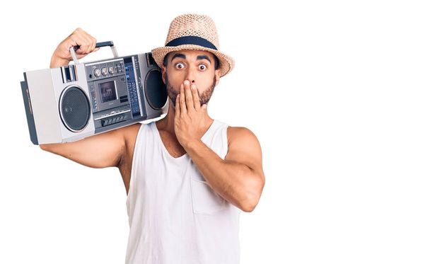 Young hispanic man holding boombox, listening to music covering mouth with hand, shocked and afraid for mistake. surprised expression  - Photo, Image